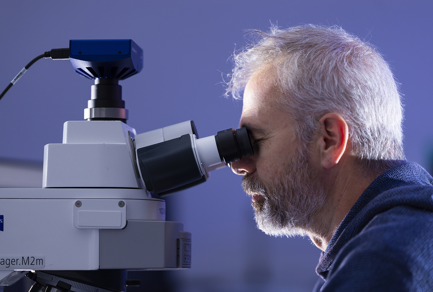 A close up of a man with grey hair looking into a microscope.