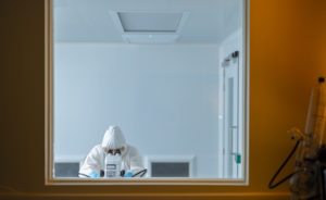 A person in full PPE looking at a microscope in a Clean Room environment
