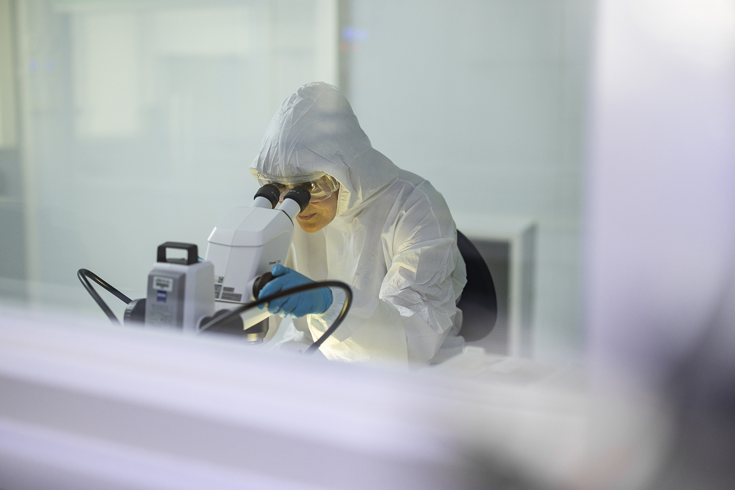 Person in full PPE looking down a micrscope