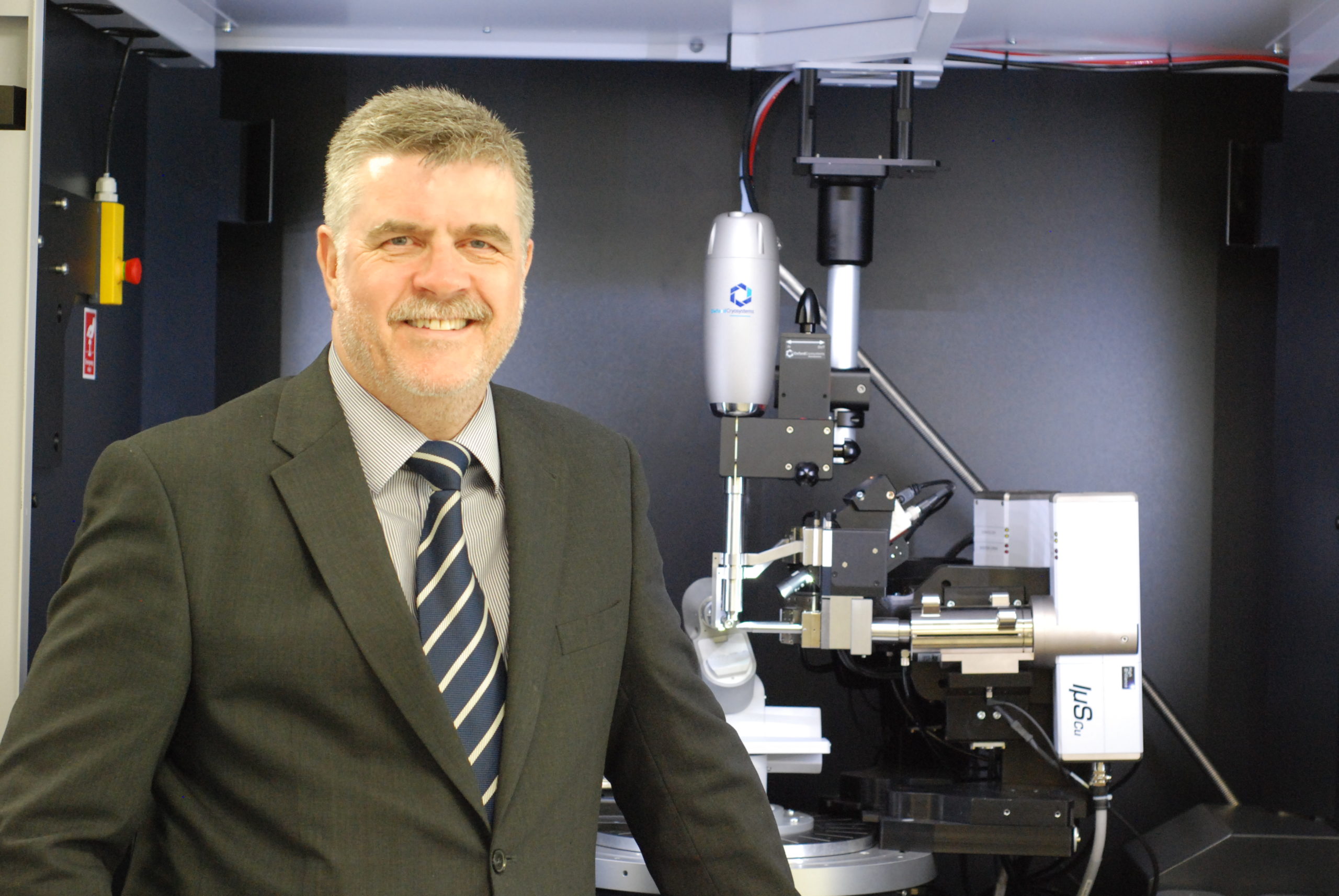 A man in a grey suit stood in front of a microscope