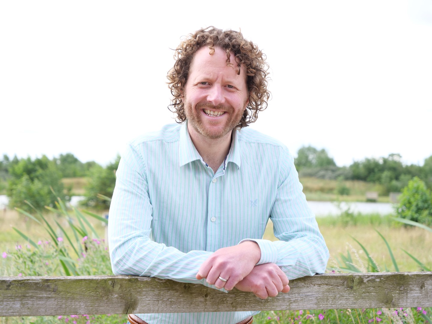 A smiling man looking over a fence with a field behind him